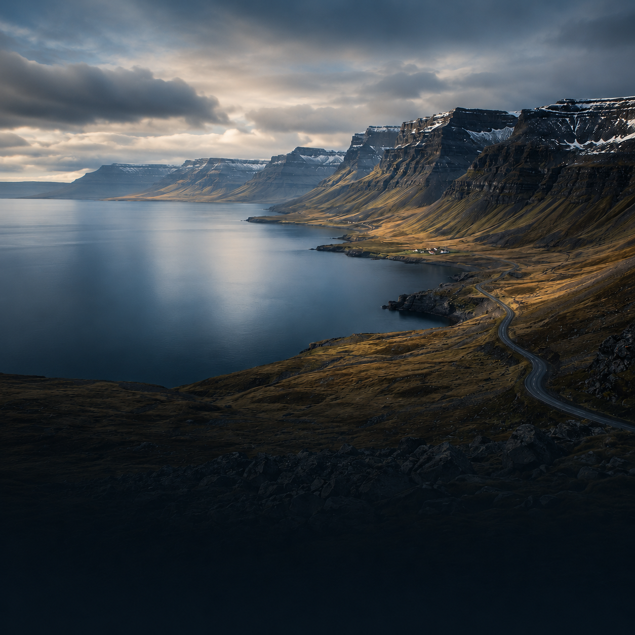 Fjordküste mit steilen Bergen und kurviger Straße in den Westfjorden Islands
